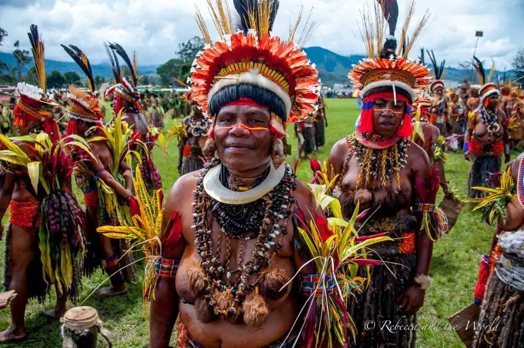 A group portrait of festival participants in Papua New Guinea, smiling in their vibrant traditional attire with feathered headdresses and colourful body paint. The lush, green background emphasises the communal and celebratory atmosphere. The Goroka Show is the biggest Papua New Guinea festival, with people coming from far and wide to participate in a singsing.