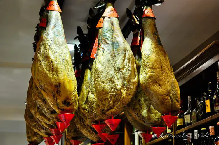 Large legs of ham hanging from the ceiling of a pintxos bar in San Sebastian. Each has a red cap at the bottom to catch liquid.