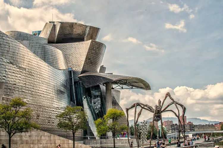 The iconic Guggenheim Museum Bilbao, with its innovative titanium-clad structure, alongside a massive spider sculpture, representing the city's fusion of contemporary art and avant-garde architecture.