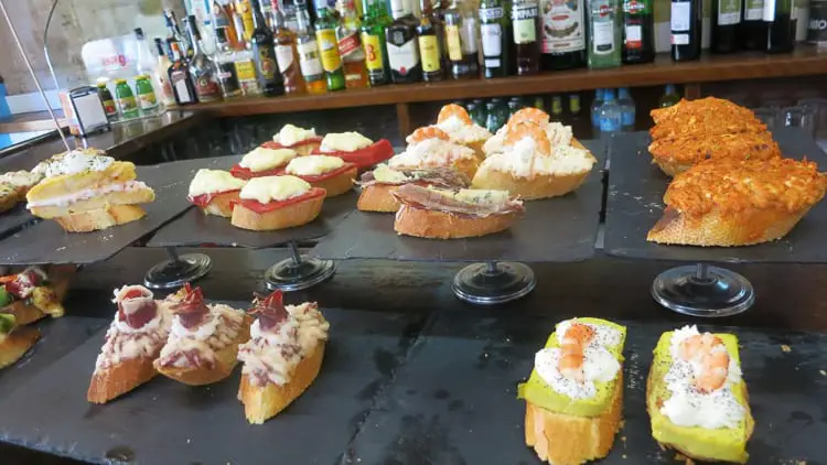 A variety of pintxos, traditional Basque tapas, creatively topped with cheeses, meats, and seafood, presented on a bar counter, showcasing Bilbao's rich culinary culture. One of the best things to do in Bilbao is try all the different pintxos.