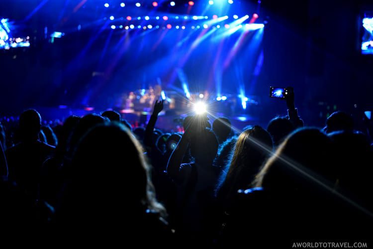 A live concert scene with a crowd of spectators illuminated by stage lights and a smartphone camera capturing the moment, reflecting the vibrant nightlife and entertainment options in Bilbao.