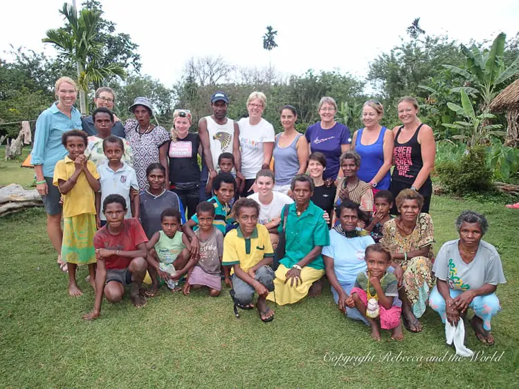 A group photo of hikers and local villagers, including children and adults, all gathered together on a grassy field. The group is smiling and appears to be enjoying each other's company in a communal setting. This was our final night on the Kokoda Track.