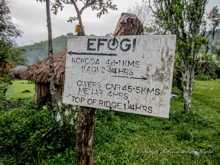 A weathered sign in the village of Efogi with directions and distances to various locations along the Kokoda Track, including Kokoda, Kagi, Owers Corner, Menari, and the Top of Ridge.