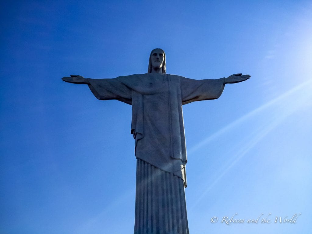 The iconic Christ the Redeemer statue against a clear blue sky. The statue is centered in the image, with arms spread wide. Visiting Christ the Redeemer is one of the most iconic things to do in Rio de Janeiro.