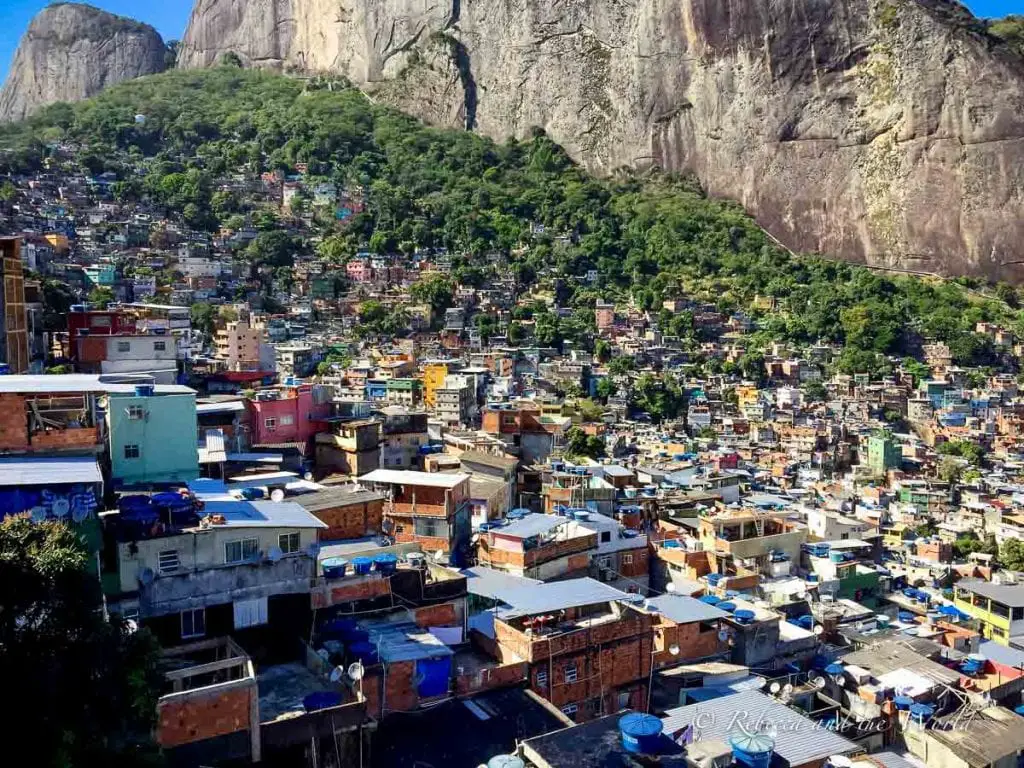 An aerial view of a densely populated area with numerous closely packed houses. The buildings are of various colors, and a large rock formation rises in the background. Taking a favela tour in Rio de Janeiro is a popular thing to do - but it's not for everyone, so think about whether you want to include this in your 3 days in Rio de Janeiro itinerary.