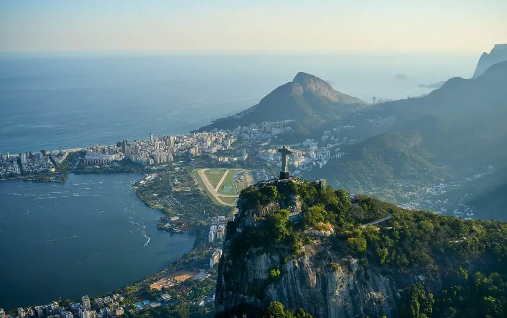 An aerial view of Rio de Janeiro. The urban area is dense with buildings, surrounded by green hills and mountains. Rio de Janeiro is one of the most beautiful cities in the world.