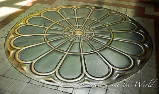 Ground floor view of a decorative circular floor design, resembling a flower or sunburst pattern, with alternating shades of green and gold metallic finishes. This is one of the intricate details of the Palacio Barolo building in Buenos Aires.