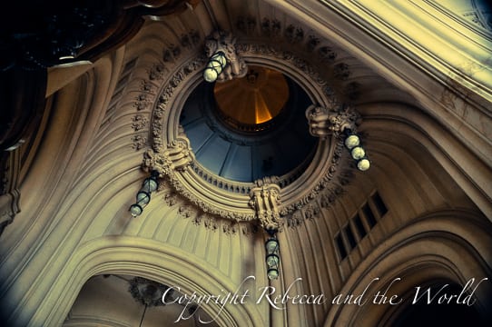 Interior view of the upper part of Palacio Barolo with a focus on a circular dome with a hanging lantern. The surrounding walls have detailed moldings and embellishments.