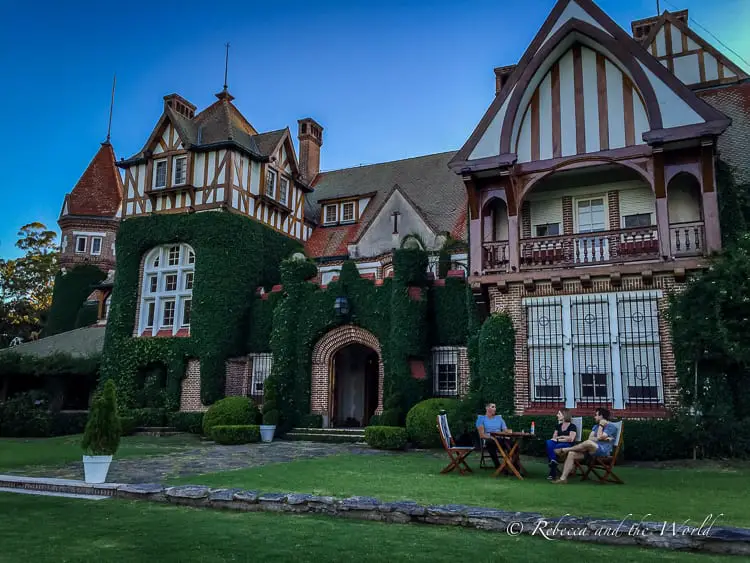 An elegant Tudor-style manor house with extensive ivy growth on the façade, with people seated outside, enjoying a conversation at dusk. The property is Estancia Villa Maria, the author of this article's favourite estancia near Buenos Aires.