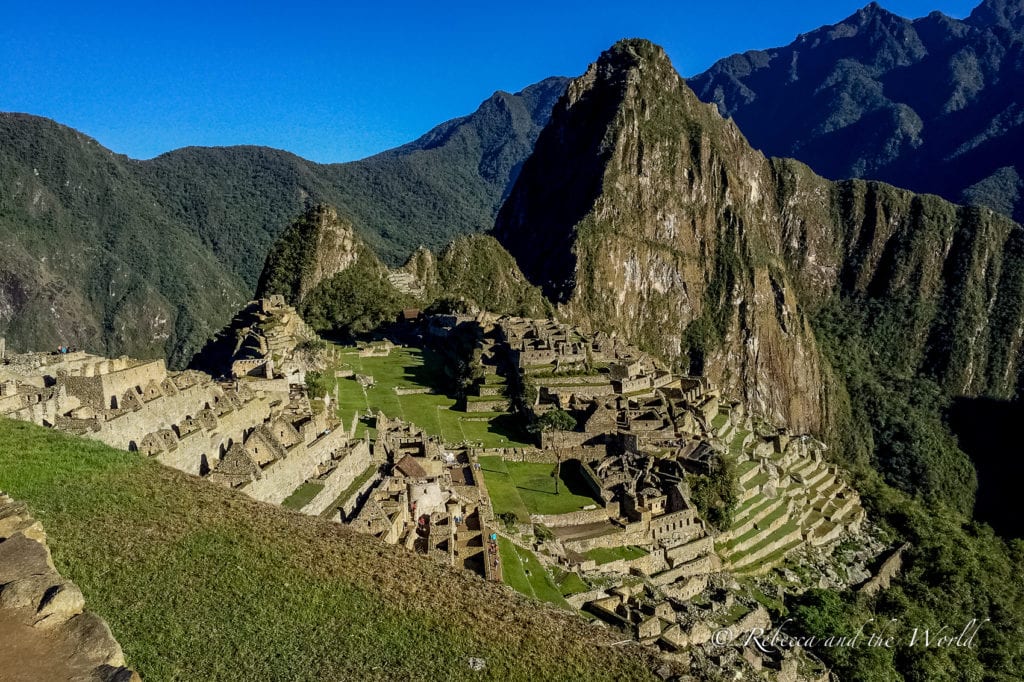 The ancient Inca city of Machu Picchu in Peru, perched on a mountain ridge with terraced fields and stone structures, under a clear blue sky.