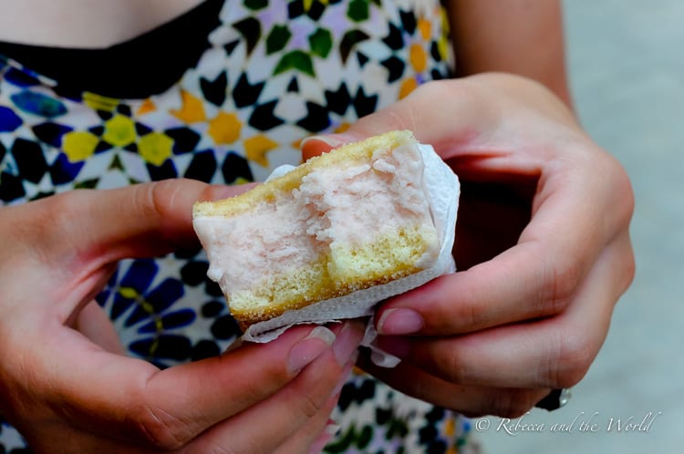A person holding a slice of Cuban ice cream sandwich, showing the fluffy, light pink ice cream sandwiched between two layers of sponge cake.