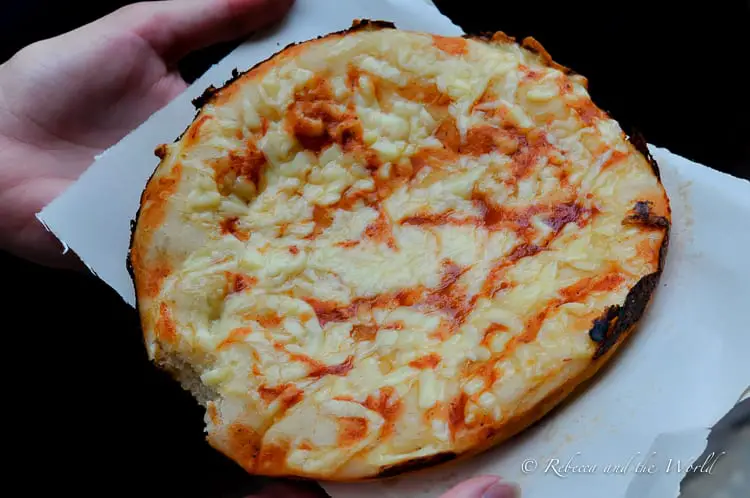 A close-up of a Cuban "pizza" topped with melted cheese and tomato sauce, held in two hands.