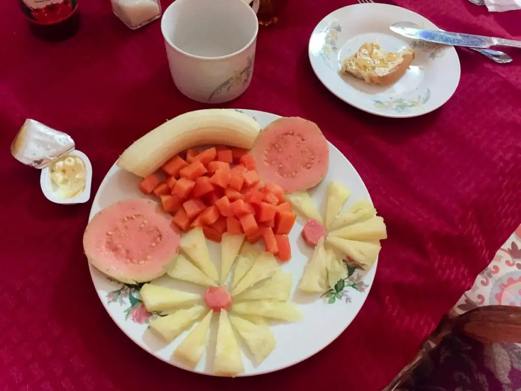 A breakfast plate featuring an assortment of fresh fruits and vegetables, including a whole banana, slices of guava, diced papaya, and pineapple arranged decoratively.