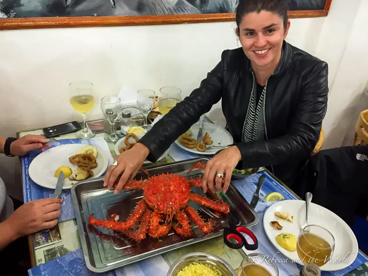 A woman - the author of the article - preparing to eat a large, red crab at a table with dining companions, glasses, and dishes of food. One of the things to do in Ushuaia is try centolla or king crab.