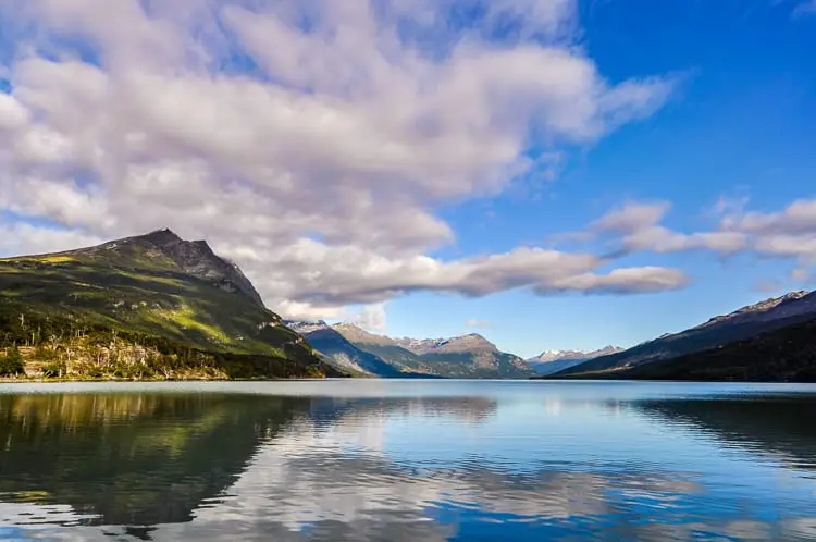 A serene lake surrounded by forested mountains under a sky with scattered clouds. One of the best things to do in Ushuaia, Argentina, is to visit Tierra del Fuego National Park.