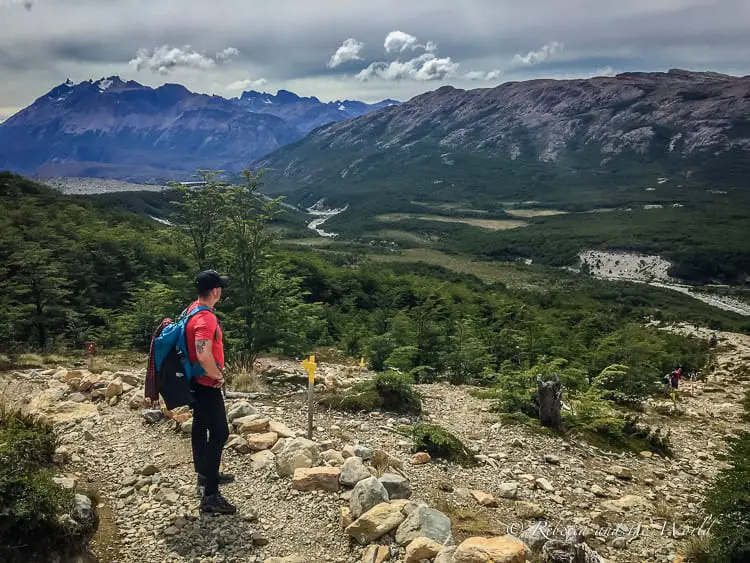 Why visit Argentina? Outdoor adventures. The lure of El Chalten's hiking trails draw trekkers from all around the world. A man in a red shirt and blue backpack surveys the views from the top of a rocky hill as he walks the trek to Mount FitzRoy in El Chalten, Argentina