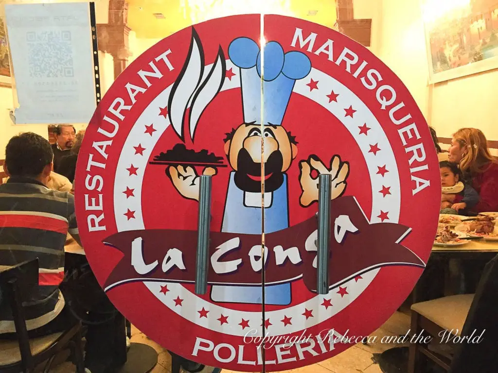 A circular red sign with a caricature of a chef holding a skewer, for "La Conga" restaurant, with patrons dining in the background. There are many international restaurants in Buenos Aires, including Peruvian restaurants.