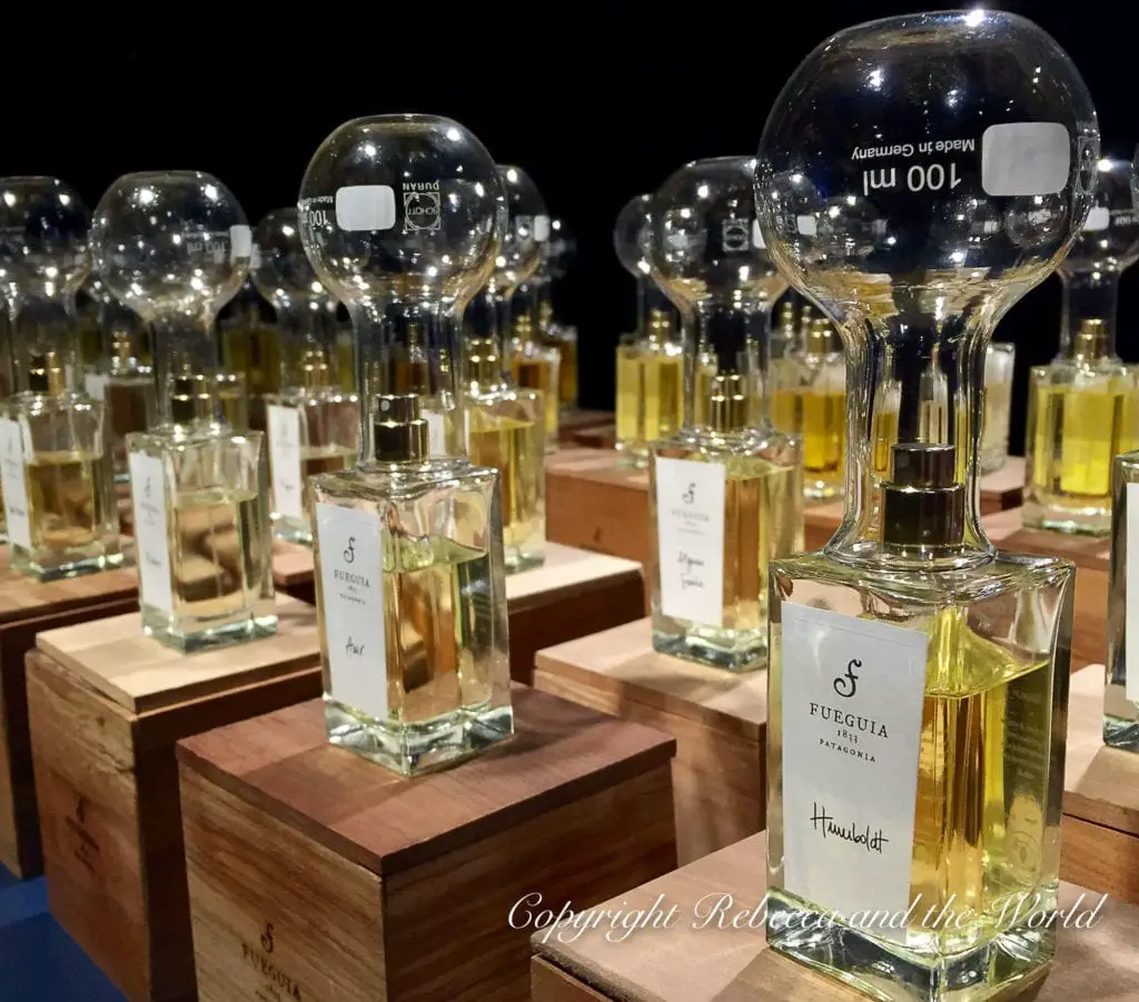 An array of spherical glass perfume bottles on wooden bases. The clear and amber-colored liquids are visible inside. Labels indicate the brand "Fueguia" and each bottle rests on individual wooden pedestals. Fueguia is a beautiful store in Buenos Aires.