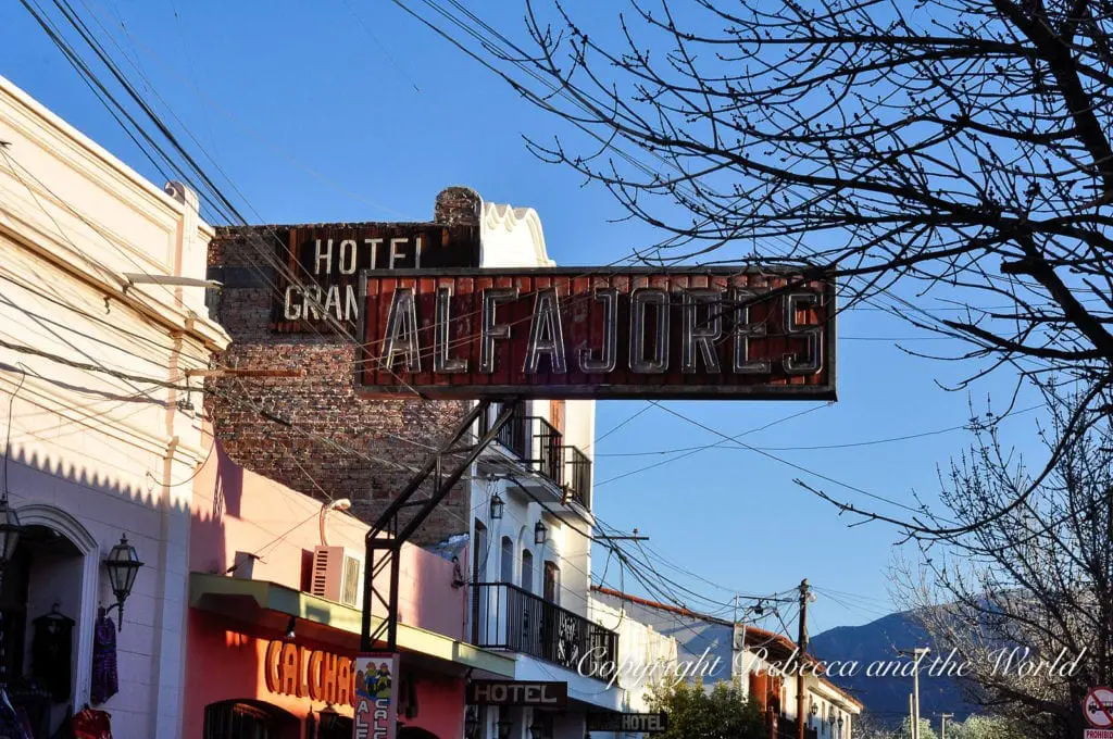 Vintage sign reading "Hotel Gran Alfajores" hanging over a street, with colorful buildings and a clear sky in the background in North Argentina. Stop in Cafayate in northern Argentina for the wine, alfajores, empanadas and wine-flavoured ice cream.