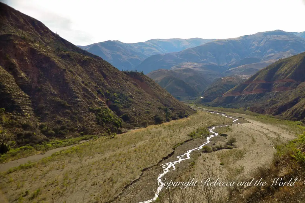 A panoramic shot of a winding valley in North Argentina with a dry riverbed snaking through, surrounded by lush green slopes and distant mountains.