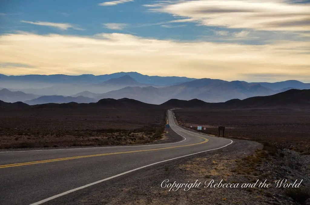 A winding road stretches into the distance through a desert landscape under a dramatic sky with layers of mountains visible in the background in North Argentina. As you travel around northern Argentina, you'll be blown away by the scenery.