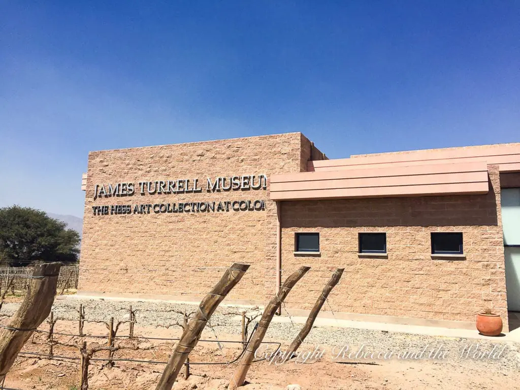 The James Turrell Museum at Bodega Colomé, a modern structure with bold lettering on the wall, standing in contrast to the rural vineyard setting around it.