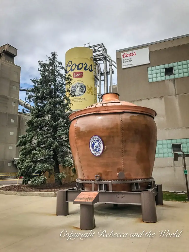 A large outdoor display of a yellow Coors Banquet beer can and a copper brewing kettle with a plaque in front, part of the Coors Brewery Complex.