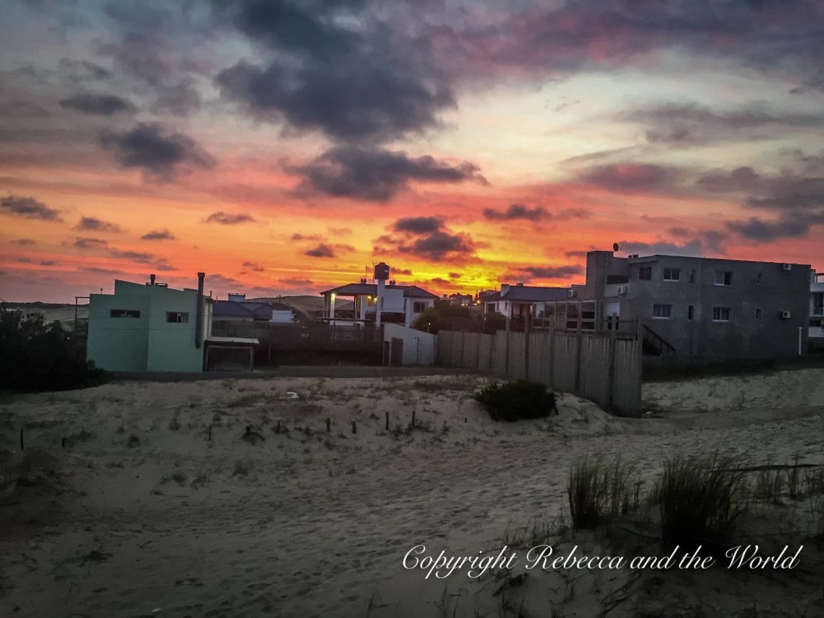 Twilight view of a beach with houses in the background, under a sky with shades of pink, orange, and blue. This sunset was captured in Punta del Diablo, Uruguay.