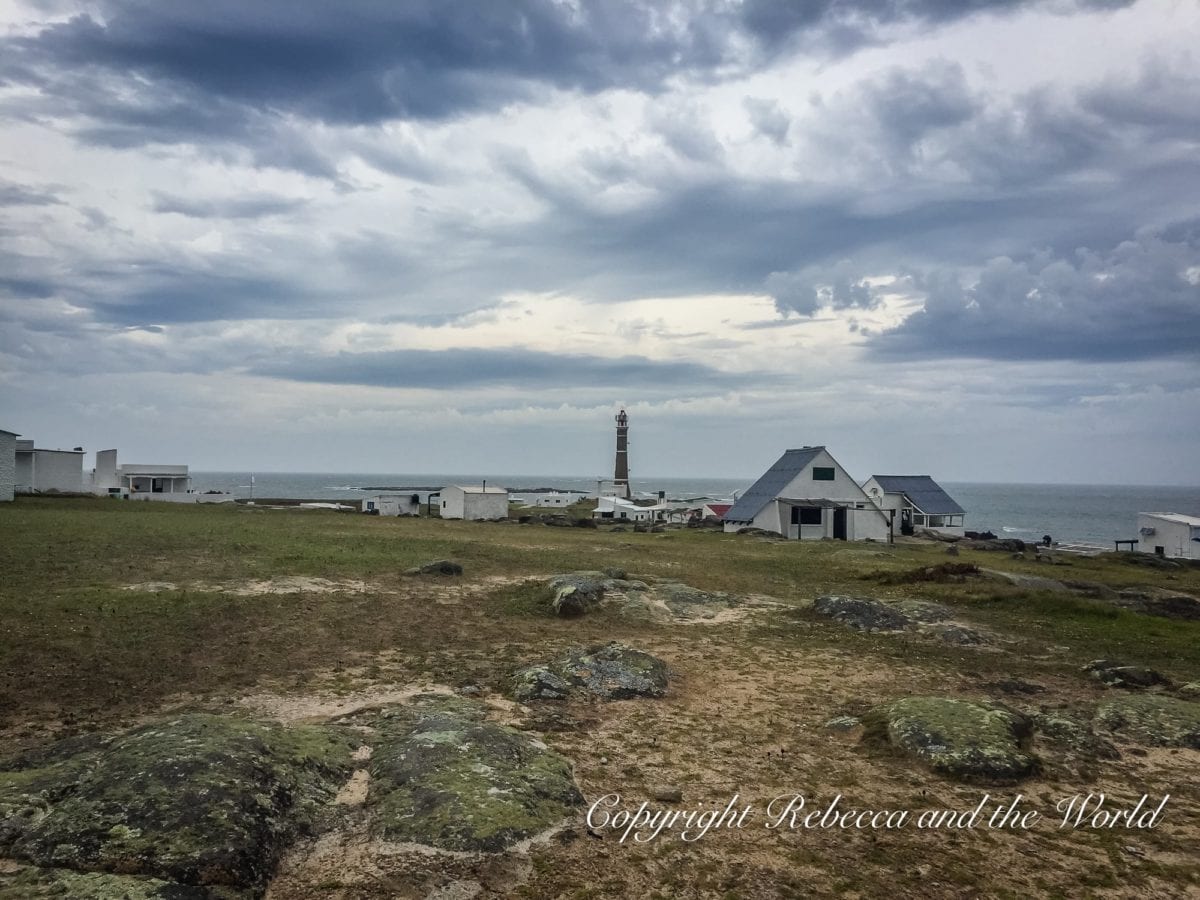 A coastal landscape with sparse vegetation, a lighthouse in the distance, and overcast skies above. Cabo Polonio is an interesting stop to add to your itinerary if you have 1 week in Uruguay.