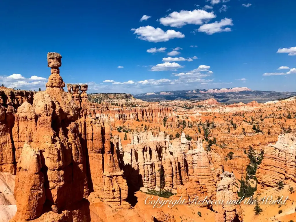A panoramic view of Bryce Canyon's intricate rock formations and hoodoos under a bright blue sky with fluffy clouds, showcasing the vastness of the landscape.