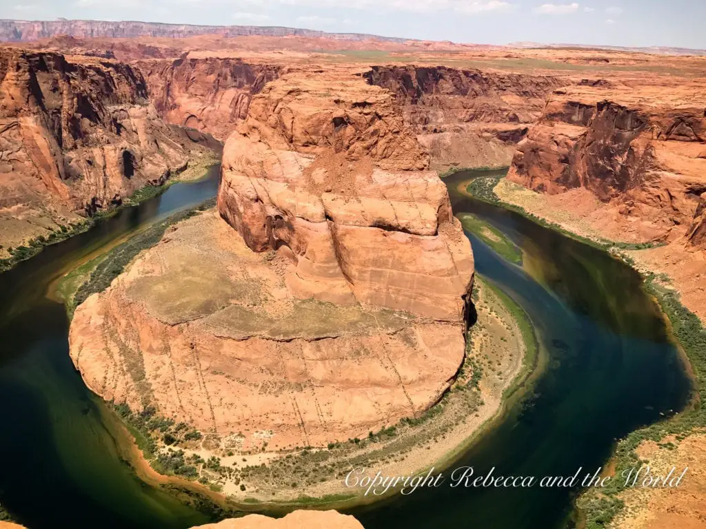 Aerial view of Horseshoe Bend, showcasing the emerald green Colorado River winding around a large, horseshoe-shaped rock formation with steep cliffs, under a clear blue sky.