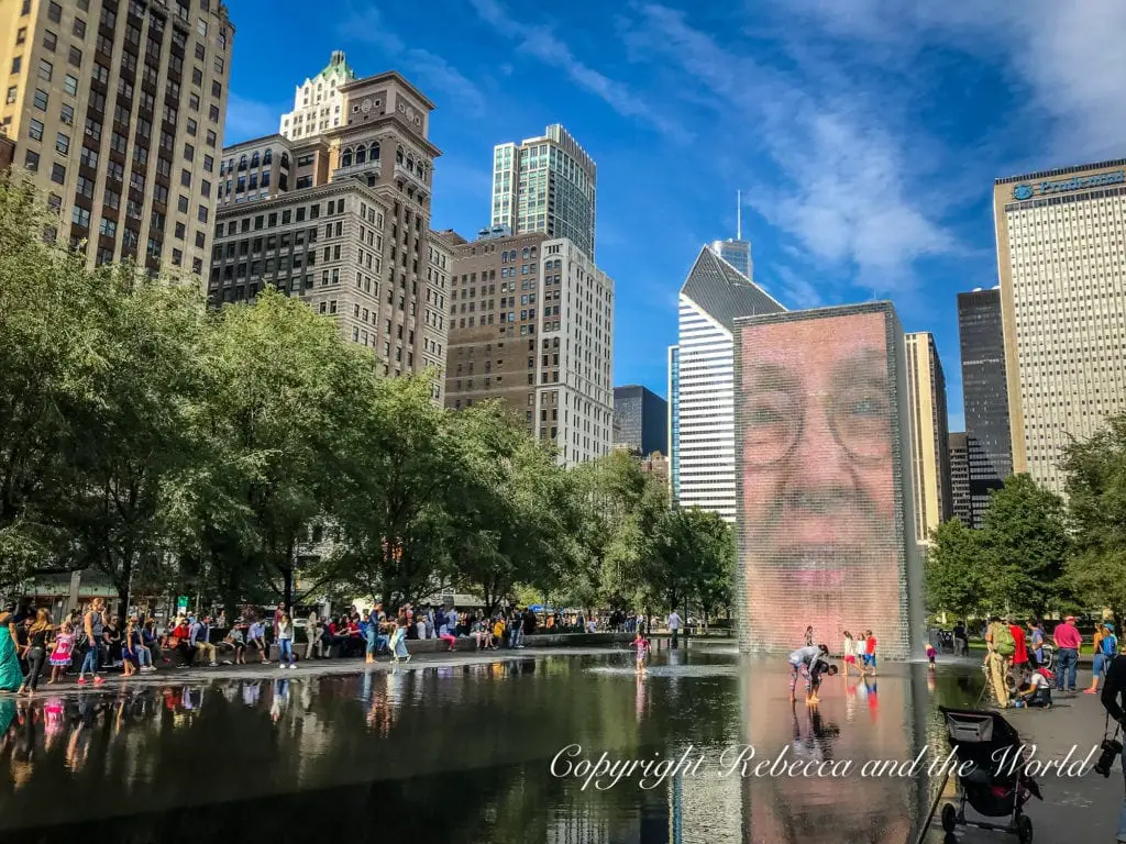 Crowds gather around the reflective surface of the Crown Fountain in Millennium Park, with a giant digital face displayed on the fountain and Chicago's skyline in the background. Millennium Park is one of the must-dos if you only have 48 hours in Chicago.