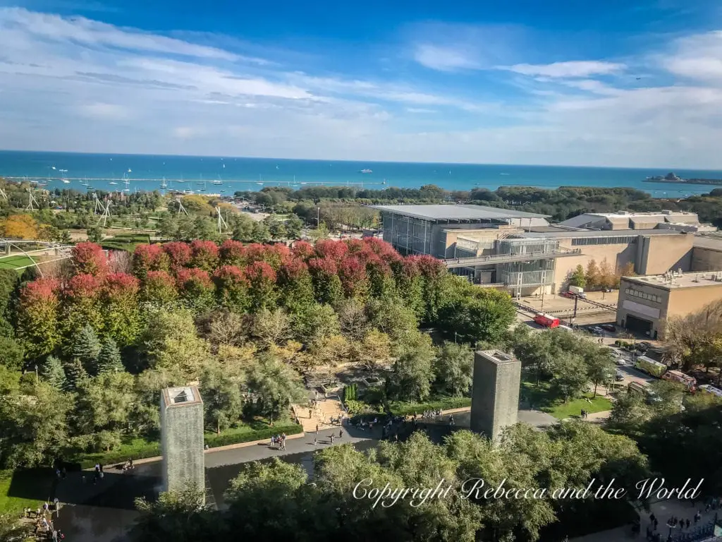 An aerial view of a lush garden in Grant Park, with colorful autumn trees, Chicago's skyline, and the blue waters of Lake Michigan in the distance.