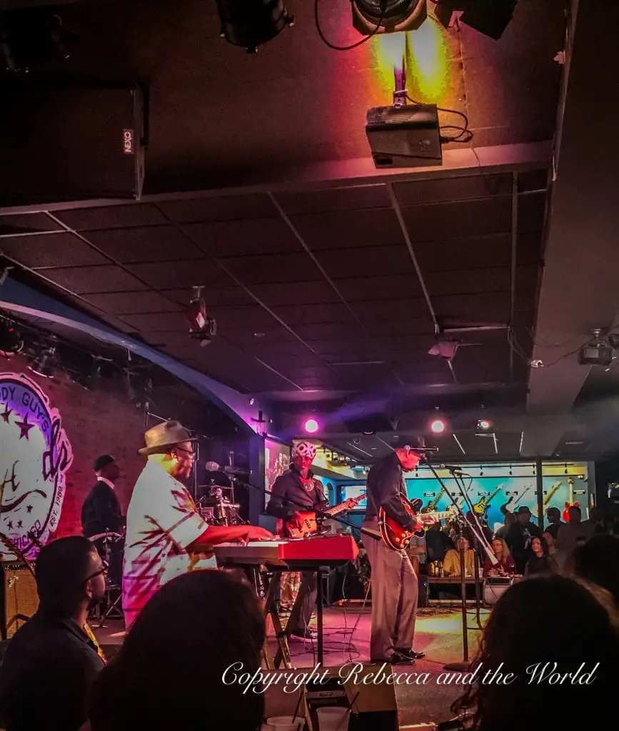 Musicians perform on stage at a blues club with vibrant lighting, spectators enjoying the live music. Buddy Guy's Legends is a great place to add to your Chicago weekend itinerary.