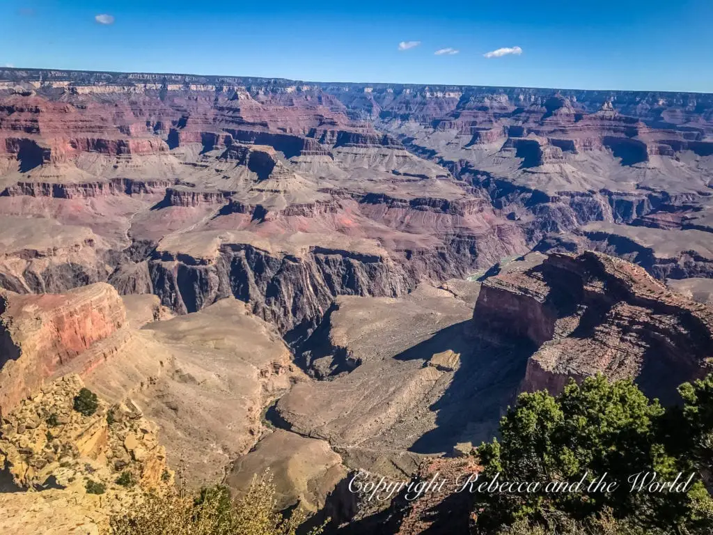 Grand Canyon panoramic view featuring prominent cliffs in the foreground and an expansive view of the canyon's intricate layers and plateaus stretching into the distance under a clear sky.