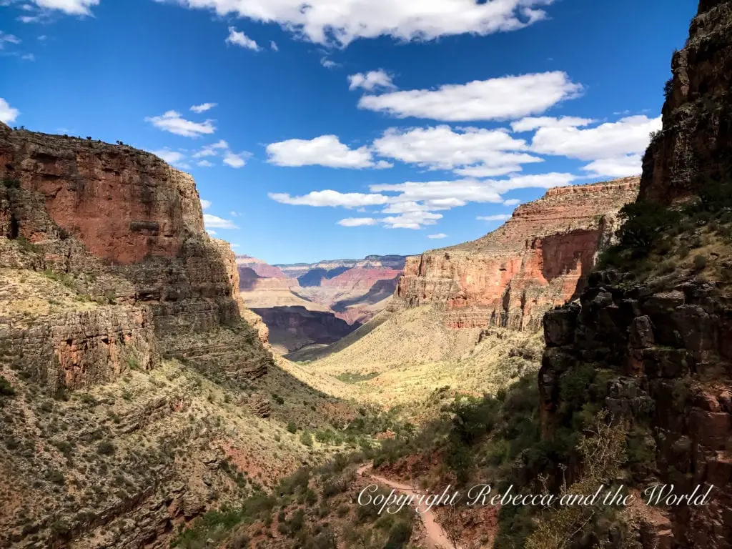 A deep gorge within the Grand Canyon under bright sunlight. The view is from within the canyon, showcasing towering rock walls and a valley that leads into the distance.