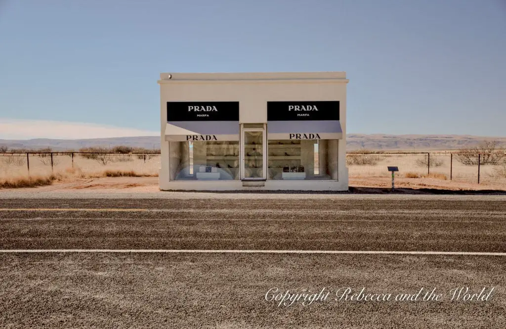 The famous Prada Marfa art installation appears as a small, solitary building with large windows displaying luxury bags and shoes, set against the vast Texas desert landscape. The Prada Marfa building is one of the best things to do in Marfa.