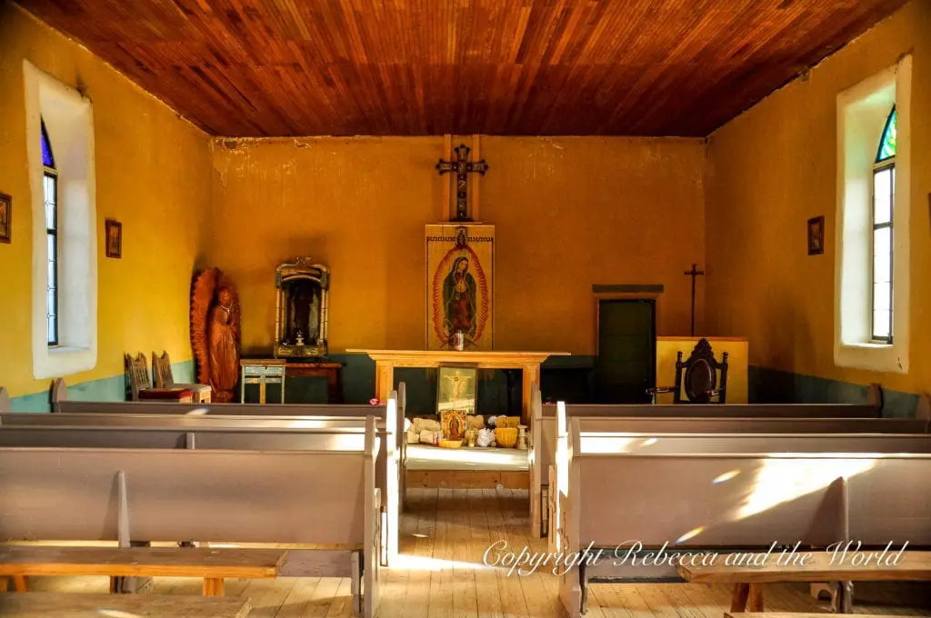 The interior of a rustic, warmly lit chapel in Terlingua, Texas,with wooden pews, religious icons, and a simple altar, conveying a sense of peaceful seclusion.