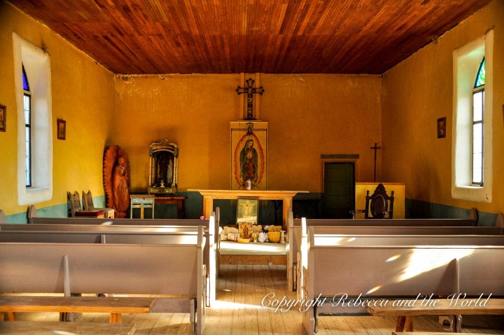 The interior of a rustic, warmly lit chapel in Terlingua, Texas,with wooden pews, religious icons, and a simple altar, conveying a sense of peaceful seclusion.