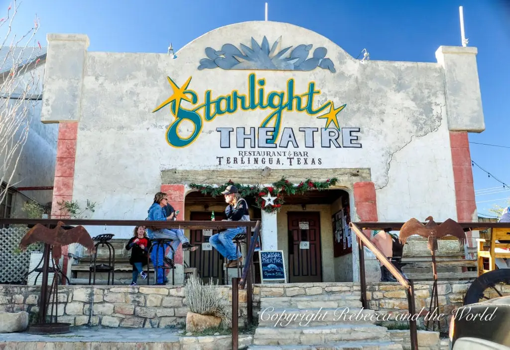 The Starlight Theatre's facade in Terlingua, Texas, with a colorful sign above the entrance, people congregating outside, and rustic metalwork on the railing.