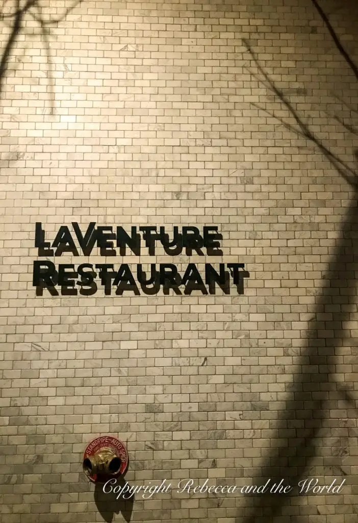 A night shot of the exterior brick wall of 'LAVENTURE RESTAURANT' with the restaurant's name in metal letters casting a shadow, hinting at a dining option in Marfa. La Venture is one of the best places to eat in Marfa Texas.