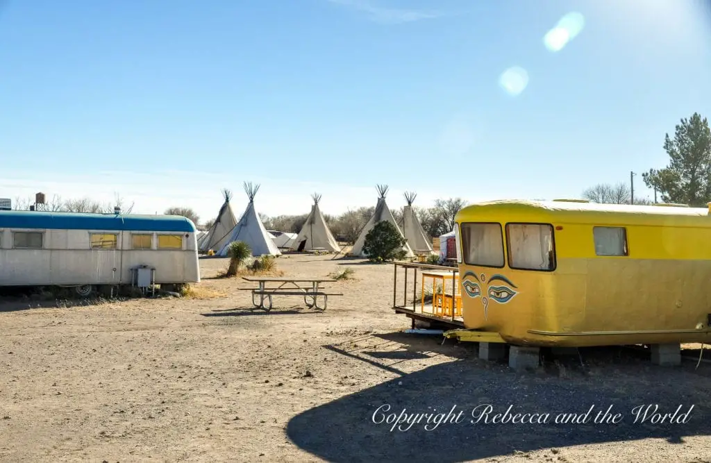 An open area with multiple retro trailers and teepees under a clear blue sky, indicating a unique outdoor accommodation experience in Marfa Texas.