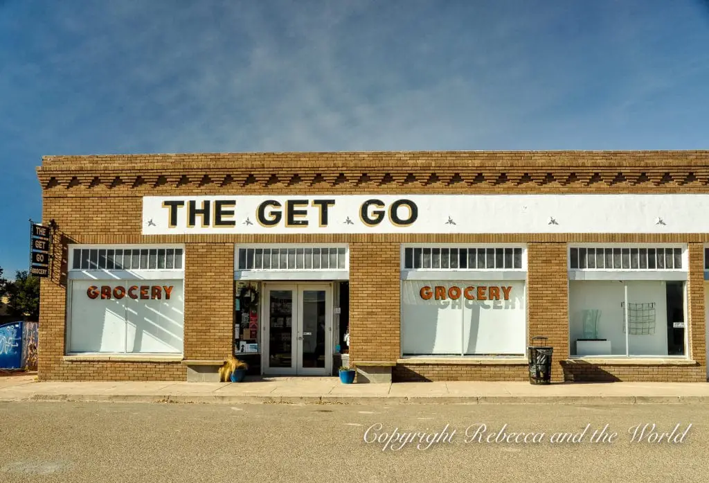 The storefront of 'THE GET GO' grocery store with large windows, an orange sign, reflecting Marfa's local businesses.