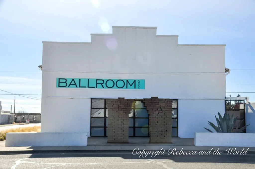 A white building with a stone facade around the entrance, featuring a teal-colored sign saying 'BALLROOM MARFA', indicative of a contemporary arts space in Marfa. Ballroom Marfa is a must-visit in Marfa Texas.