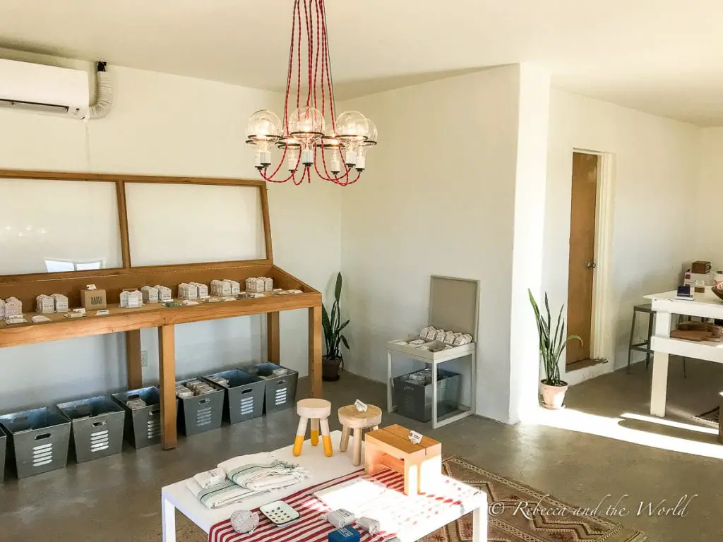 A minimalist interior of a shop with natural light, featuring a red chandelier, simple wooden furniture, and neatly organised shelves with products. Marfa Brands is one of the gorgeous places to shop in West Texas.