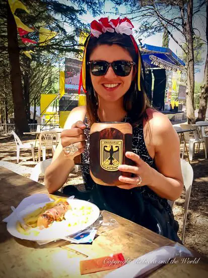 October in Argentina means Oktoberfest in some parts of the country. A woman (the author of. this article) smiles at the camera while holding a large wooden stein. She has a headband in her hair with white and red flowers. She is in Villa Belgrano in Argentina at an Oktoberfest festival.