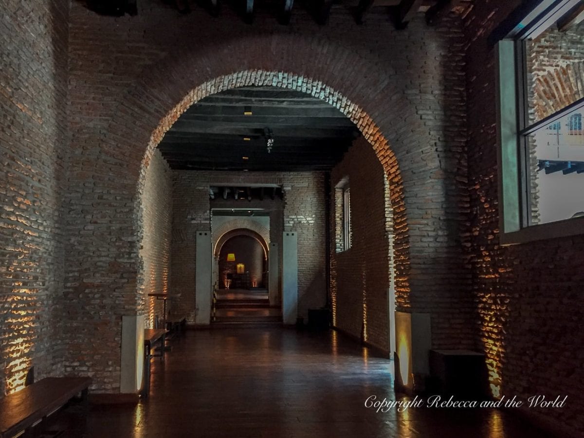 A dimly lit corridor with brick walls forming an archway leading to a series of doorways - this is El Zanjon in the San Telmo neighbourhood of Buenos Aires. The warm lighting accentuates the texture of the bricks and creates a moody atmosphere. There's minimal furniture, emphasising the architecture.