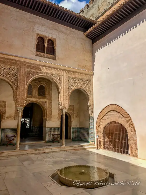 An ornately decorated archway with intricate Islamic geometric and floral motifs, leading to a courtyard within the Alhambra's palace complex.