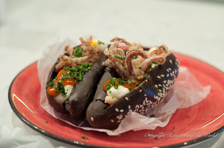 A dish on a red plate featuring black squid ink buns topped with seafood and sauce. This was one of the dishes at Tragata in Ronda, Spain.