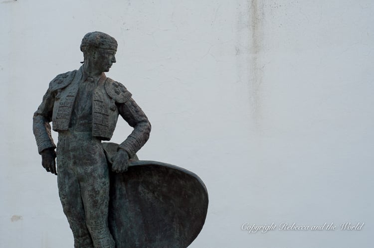 A bronze statue of a matador, in front of a plain white wall. This statue is out the front of the bullfighting ring in Ronda, Spain.